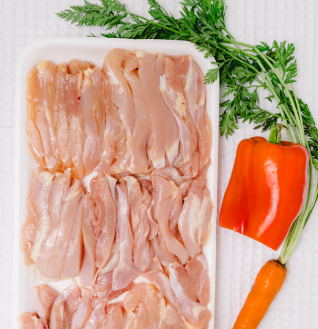 Slices of raw Chicken Fajita meat on a white tray, next to a carrot, red bell pepper, and green herbs.