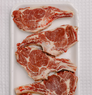 Four raw, bone-in Beef Chops displayed on a white styrofoam tray.
