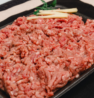 Pile of raw Beef Qeema (ground beef) garnished with ginger slices and herbs in a black tray."