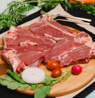 Four thick, raw Beef Cuts on a wooden cutting board, garnished with onion, tomatoes, and radish.