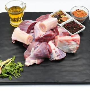 Raw Beef Nihari Cut pieces with bone marrow, served on a black platter alongside oil, spices, peppercorns, and cilantro for garnishing.