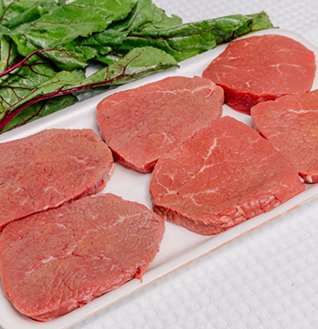 Several raw beef steaks on a white plate, garnished with fresh green leaves.