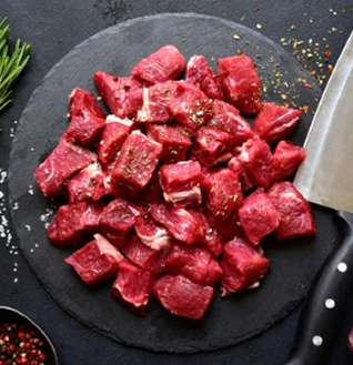 Pile of raw, boneless Lamb Leg cubes seasoned on a black round platter with a knife.