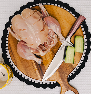 Raw Whole Chicken on a wooden cutting board with a knife and sliced cucumber.
