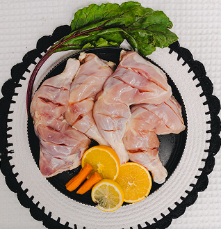 Raw Chicken Leg Quarters prepared for Tandoori, served on a black plate with orange slices, carrots, and green leaves.