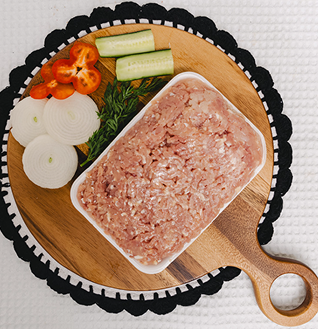 Raw Chicken Qeema (ground chicken) on a wooden cutting board, surrounded by sliced onion, cucumber, and red chili peppers.