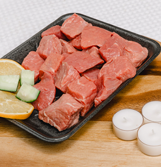 Cubes of raw Beef Boti in a black tray, garnished with lemon and cucumber slices.