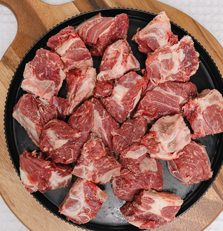 Cubes of raw Beef Eye Round on a round black platter set on a wooden cutting board.