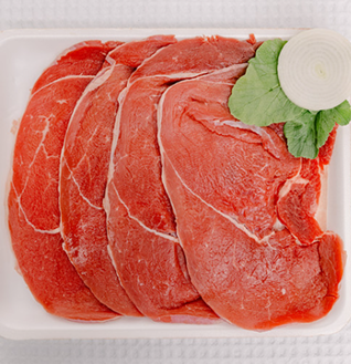 Thinly sliced raw Round Beef Steaks on a white tray, garnished with an onion slice and green leaves