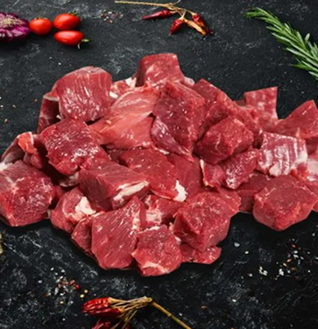 Heap of raw Lamb Shoulder Cubes on a dark background, garnished with cherry tomatoes and chili peppers.